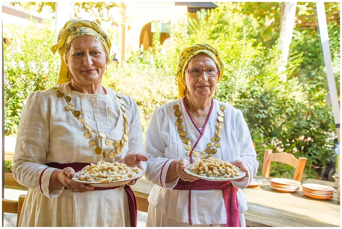 Two women offer traditional Greek snacks while wearing traditional clothes in Costa Navarino