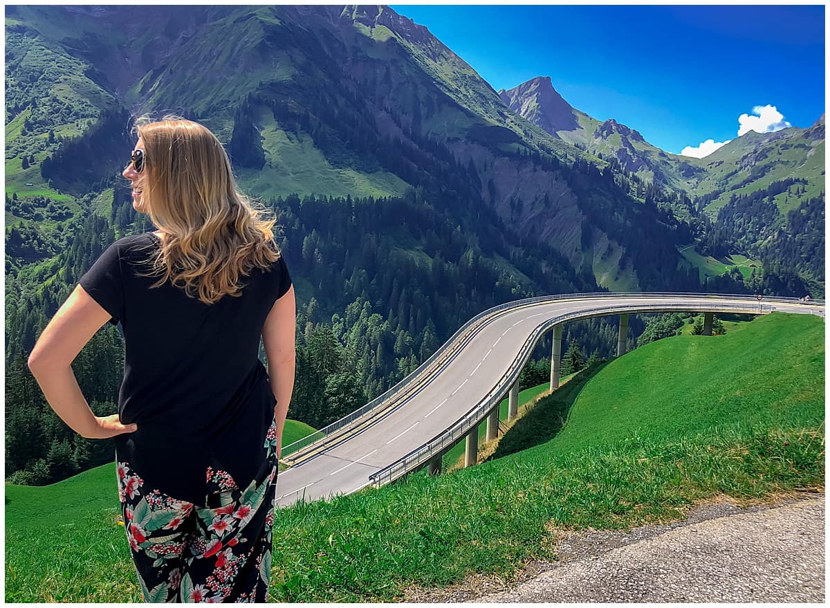 The Kasestrasse Cheese Route in Bregenzerwald Austria - Abigail King stands by the curving road with the mountains in the distance