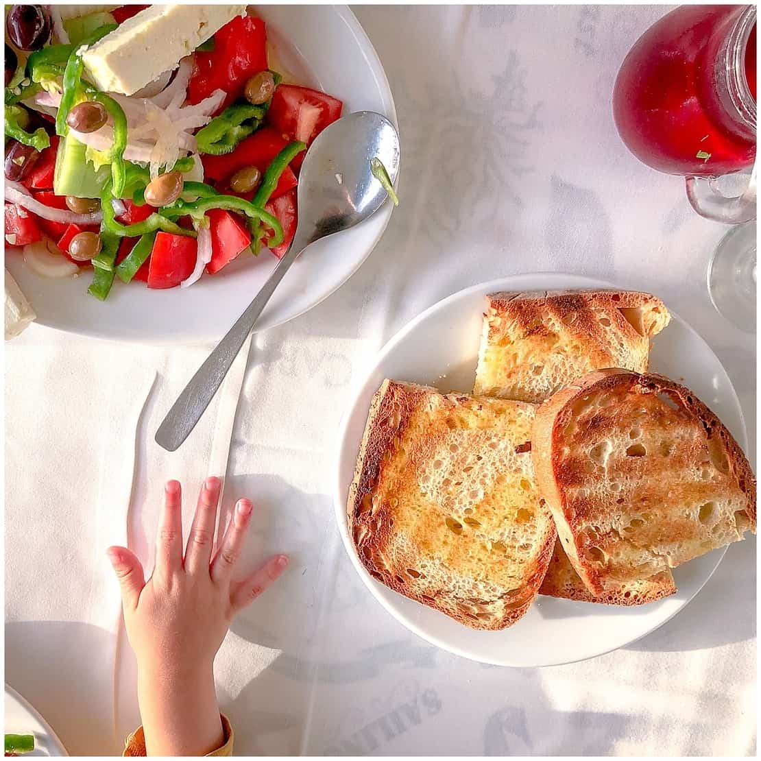 Toddler hand reaches for bread and Greek salad