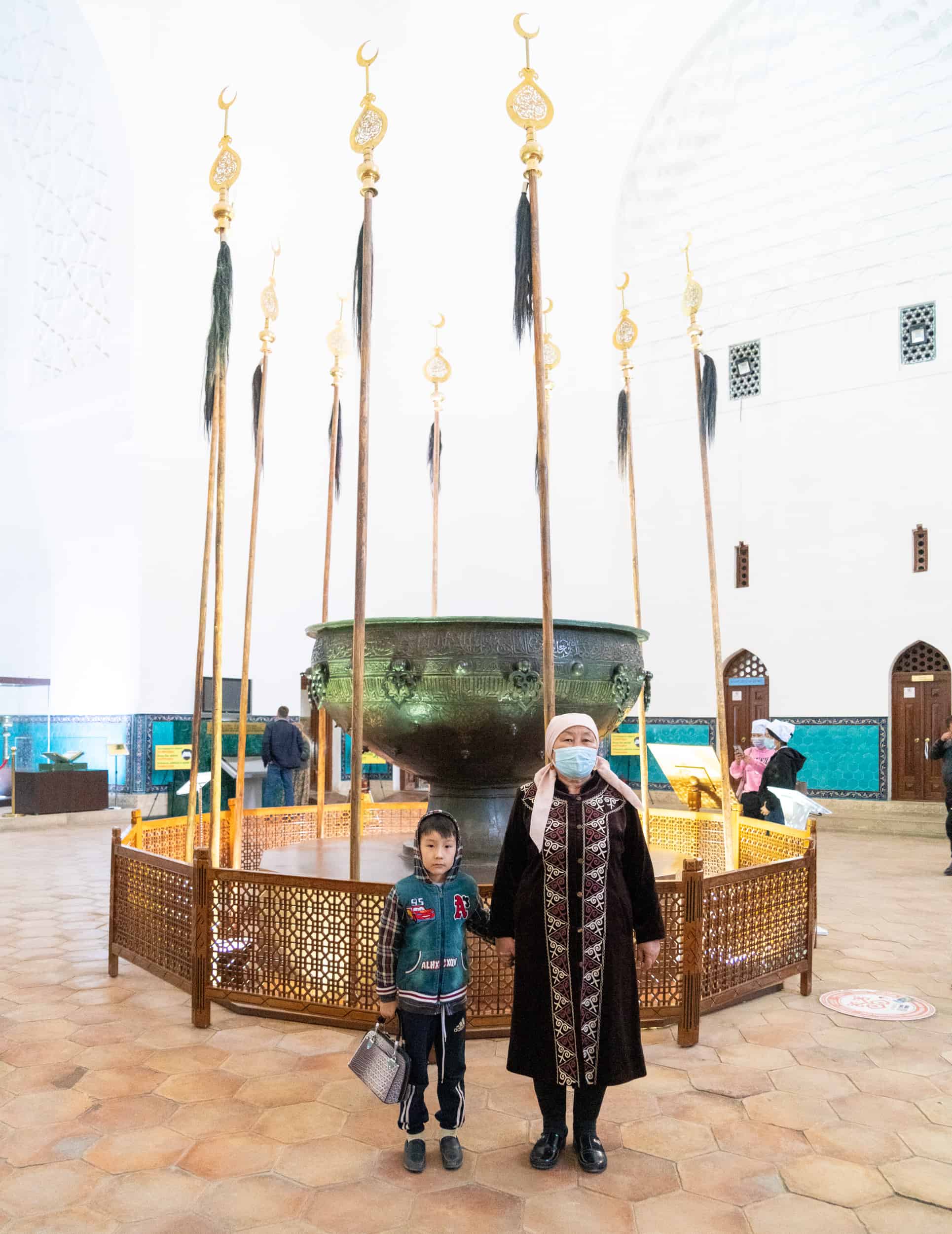 Kazakhstan - Turkistan - Mausoleum Khoja Ahmed Yasawi - Grandmother and child by large cauldron tay kazan