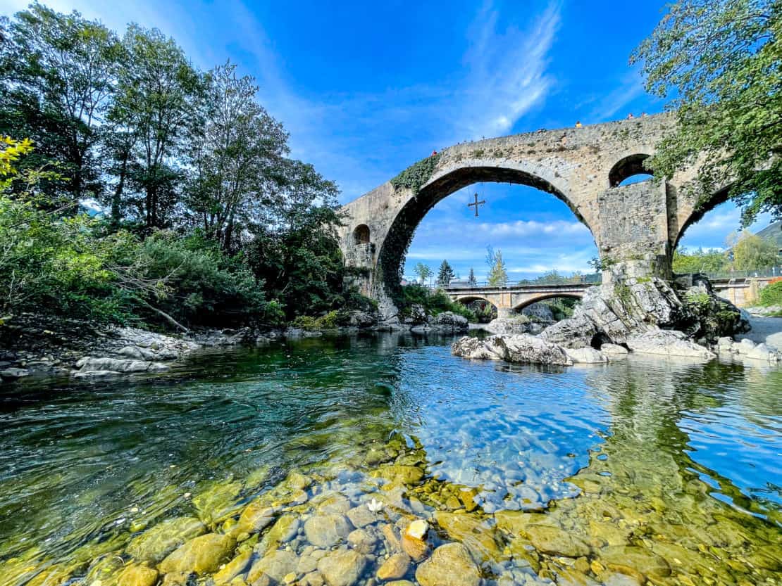 View across the water of the Roman bridge with hanging Victorian Cross in Cangas de Onis in Asturias, Spain