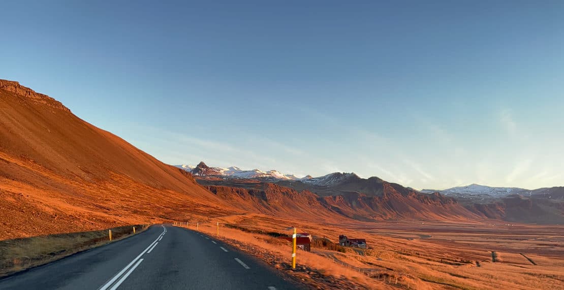 Driving along a road during sunrise in Iceland with snowy peaks in the background