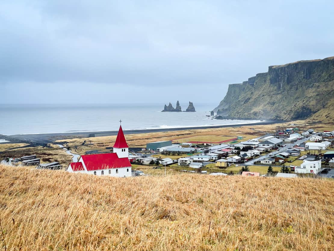 View from the mountain near Vik in Iceland showing the red roofed church and stone trolls in the sea.