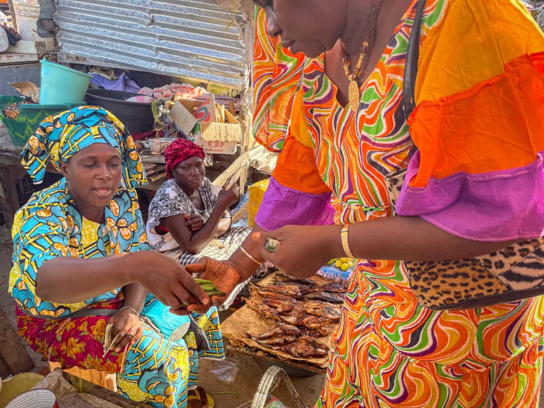 Picking up food supplies at Tanji Fishing Market - two women exchange goods for cash