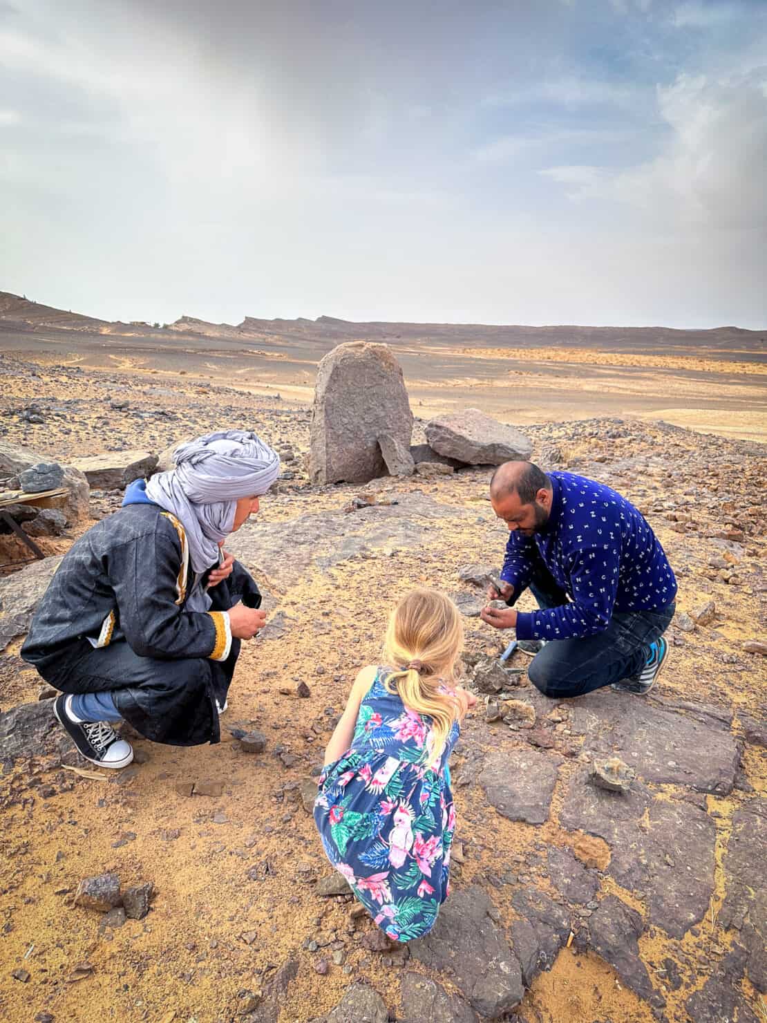 Berber men and blonde child looking for fossils in the desert near Merzouga in Morocco