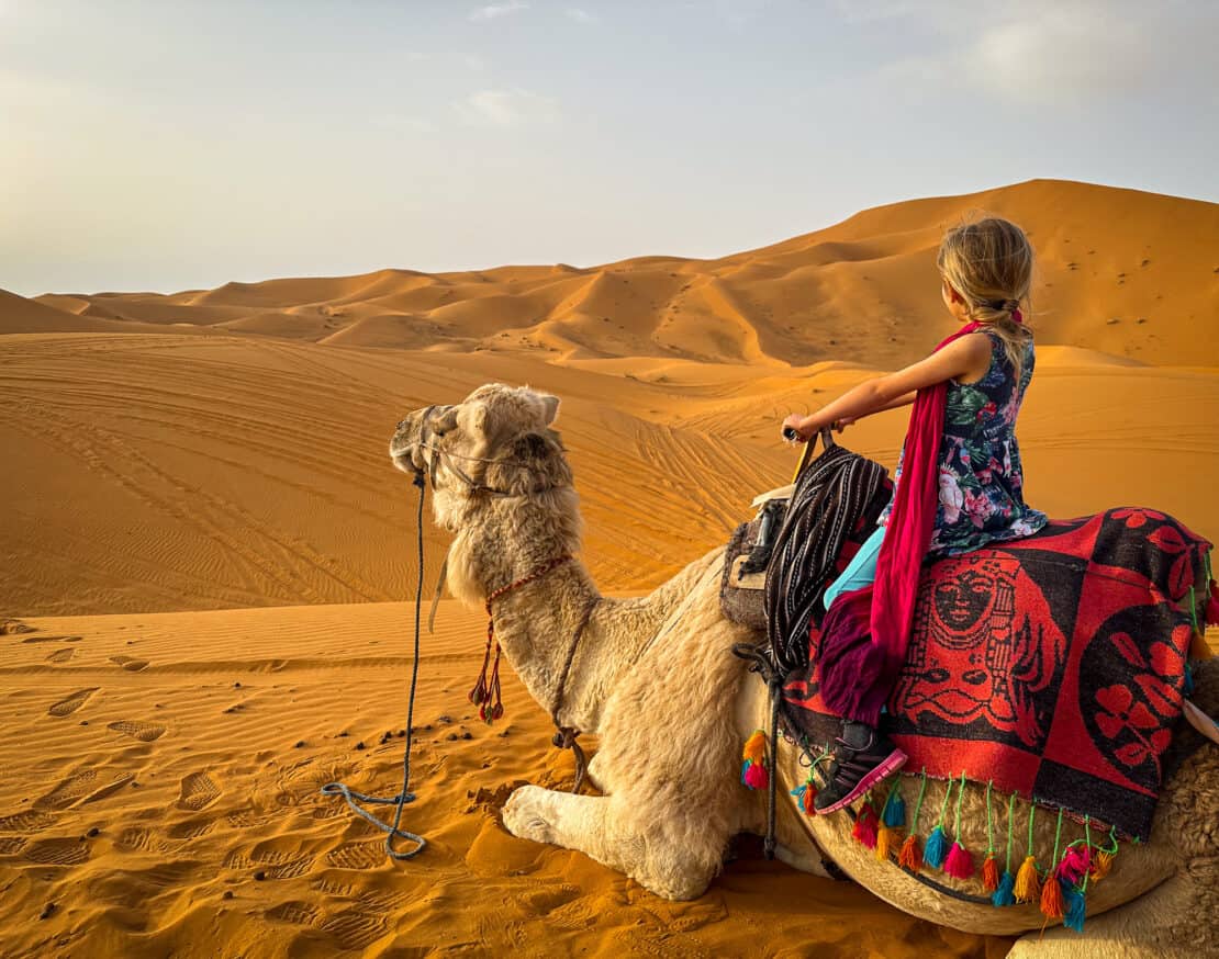 Child sitting on a camel, gazing at the dunes as a way to travel to Morocco