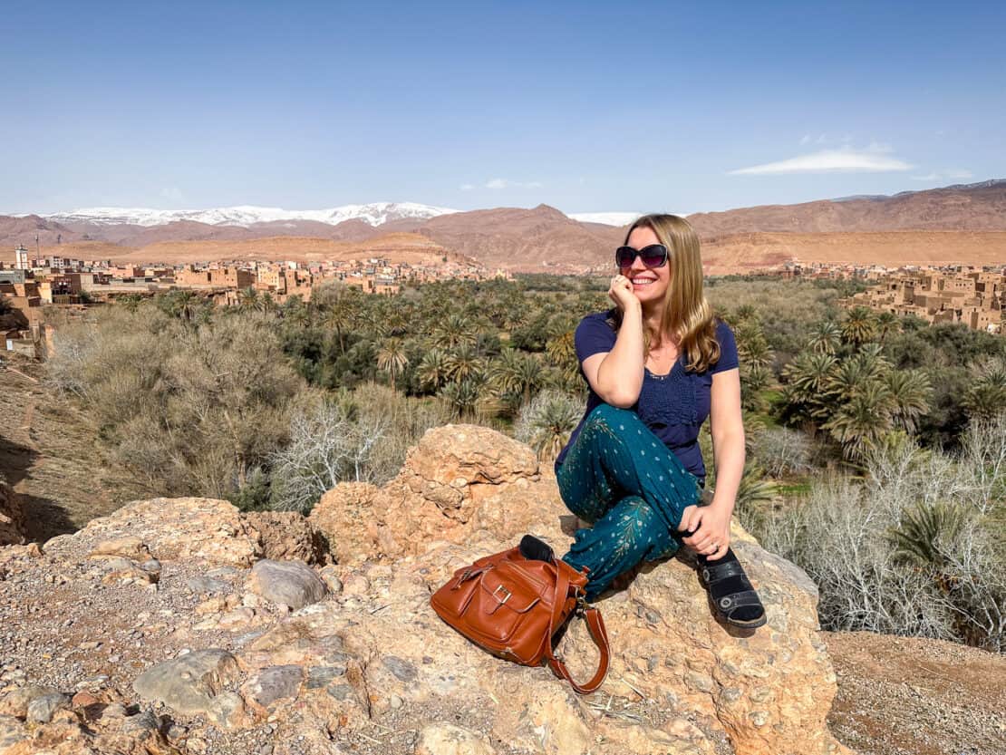 Abigail King in front of snowy mountains and palm trees en route to the Dades Gorge
