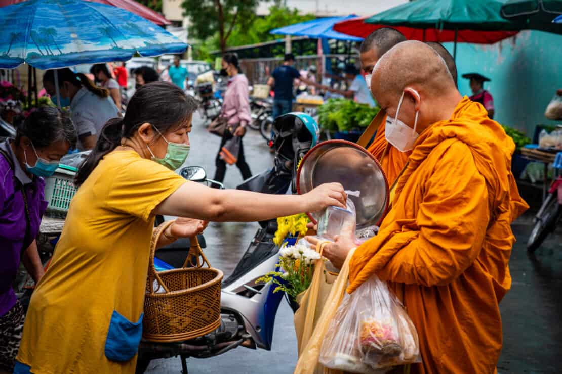 Woman giving alms to monks in Nan Thailand in the street