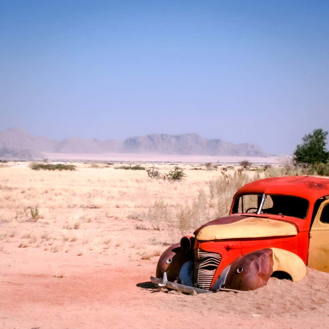 Rusting orange car abandoned in the desert