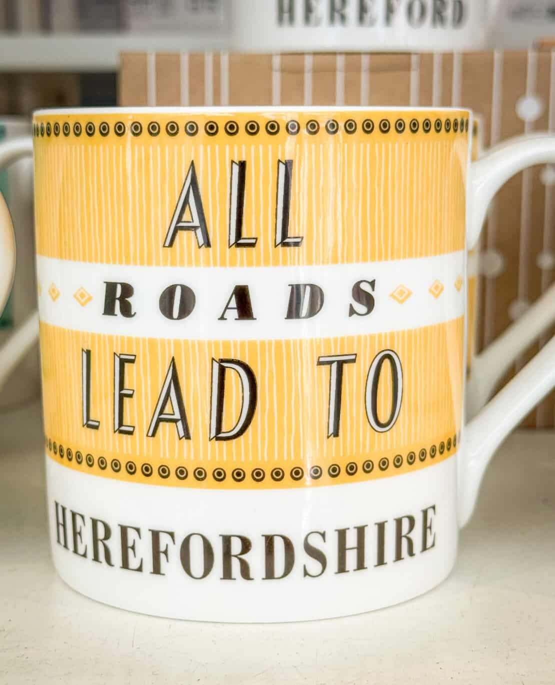 Enamel mug reading "All Roads Lead to Herefordshire" on a wooden table outdoors