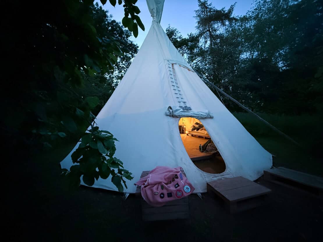 White House Glamping tipi at dusk beside the River Wye in Herefordshire, with warm lights glowing inside the canvas tent