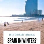 Sunny winter beach in Barcelona with people walking along the sand and the W Barcelona hotel overlooking the Mediterranean Sea